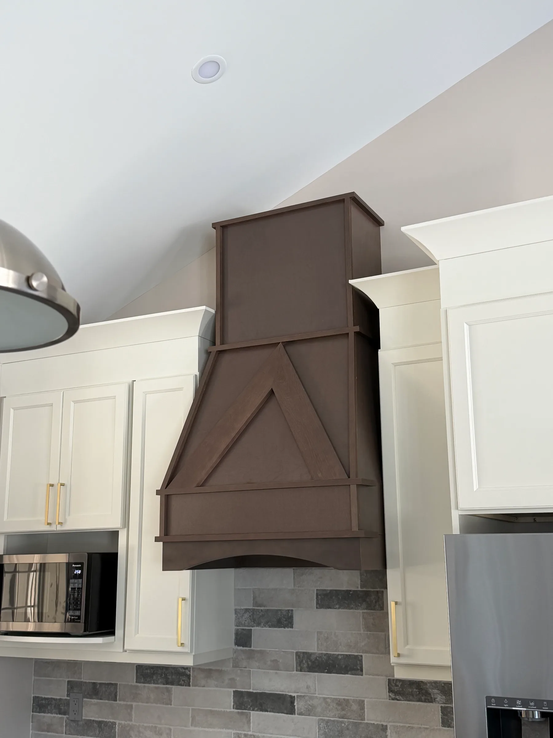Dark wood vent hood surround with white cabinetry and stacked stone backsplash